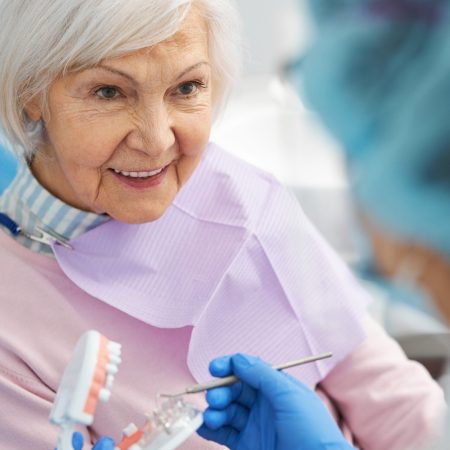 Curious retired woman staring at a dental professional while she pointing at transparent part of teeth model with probe
